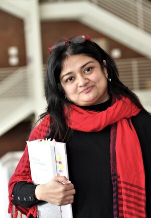 Nubras Samayeen stands in the landscape architecture building, wearing a red scarf and holding a white folder.