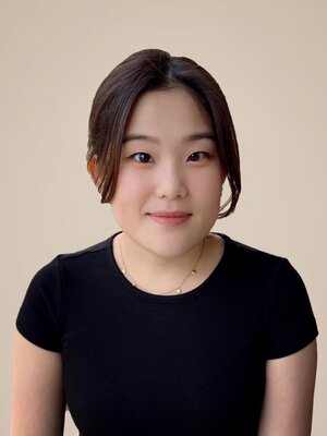 Hyeree Ellis is wearing black and smiles at the camera in front of a beige background.