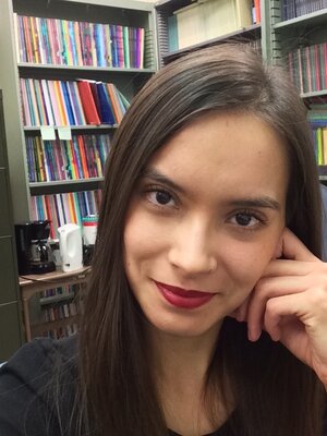 Grad student Sabrina Lee sits in an office with bookshelves behind her; she smiles at the camera