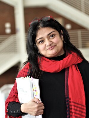 Nubras Samayeen stands in the landscape architecture building, wearing a red scarf and holding a white folder.