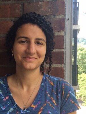 Grad Student Claire Baytaş stands outside against a brick wall and smiles at the camera.